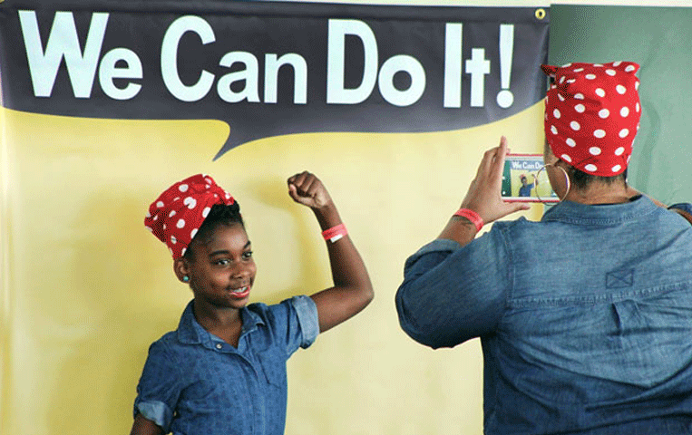 Girl takes photo in front of the “We Can Do It” sign at Rosie the Riveter/WWII Home Front National Historical Park (NPS)